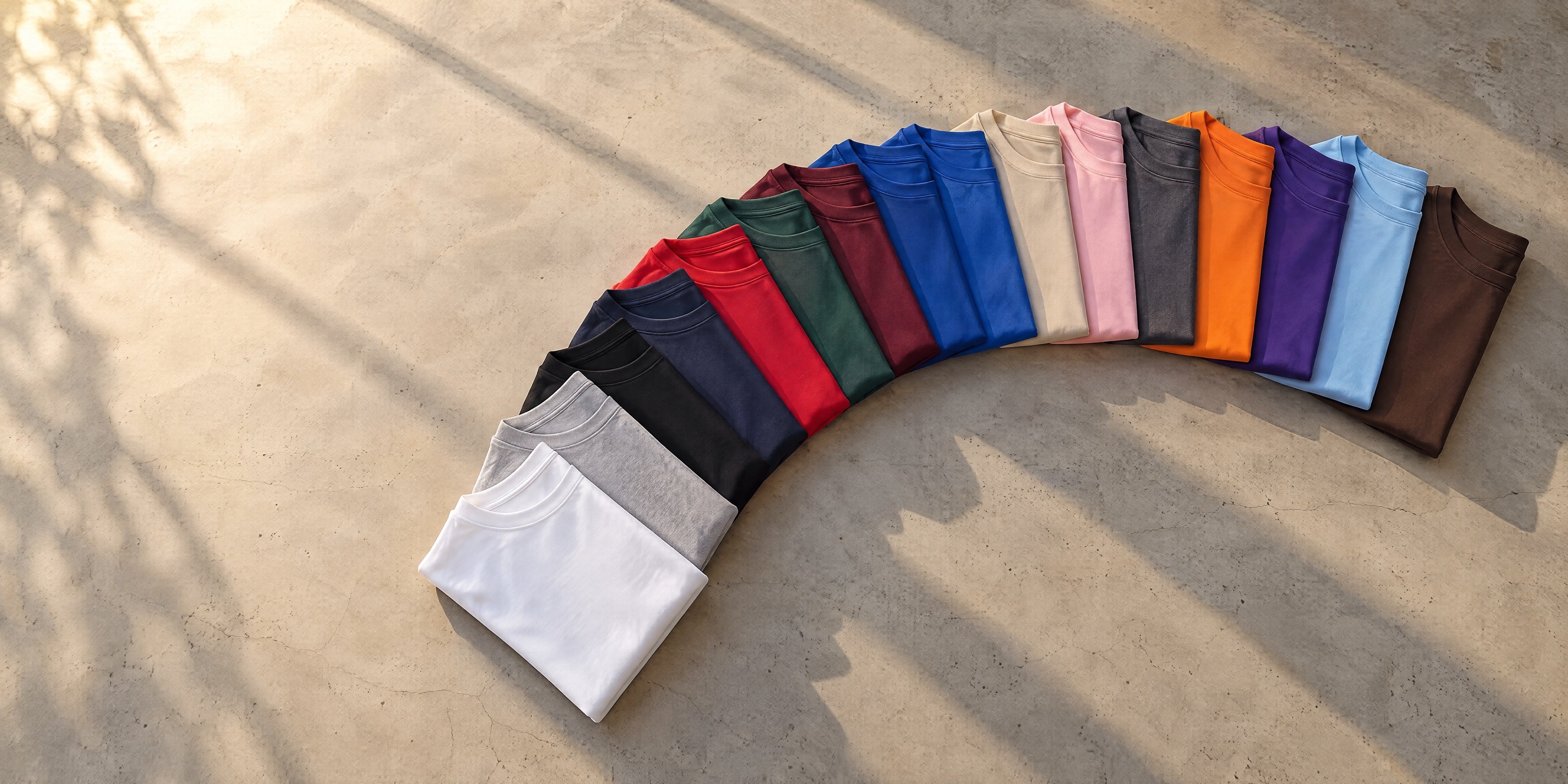 A flat case opening into a fanned arc of folded blank T-shirts in every stocked colour.